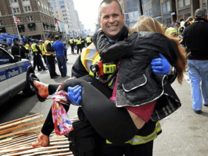 Photograph of a first responder carrying a victim from the Boston Marathon with a scarf tied around her leg (with no windlass this is not a tourniquet)