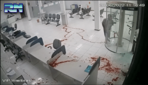 A security video still showing a lobby with desks covered with spurting blood and a clear trail of blood leading to a suspect about to die from blood loss by the revolving door